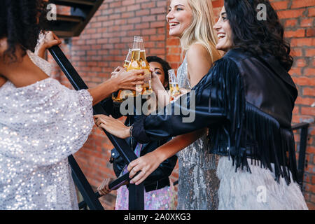 Il gruppo di donne aventi le bevande insieme. Amici di sesso femminile la tostatura con bottiglie di birra mentre passeggiate in città. Foto Stock