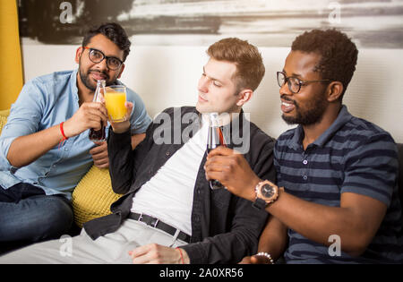 Maschio felici amici appassionati di calcio guardare partite di calcio in tv e celebrare il traguardo di bere succo di frutta e acqua frizzante seduti sul divano di casa. Amicizia, s Foto Stock