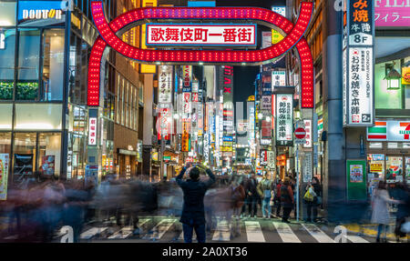 Vista panoramica di una persona che fa le foto, Motion blured gente camminare attraverso l'entrata di Kabukicho intrattenimento e il quartiere a luci rosse di Tokyo Foto Stock