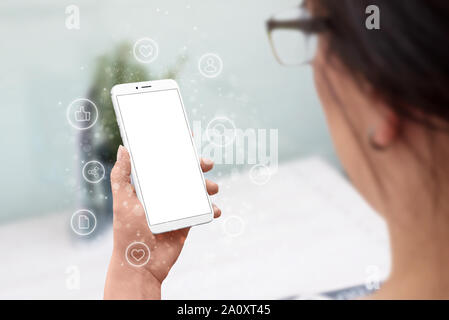 Donna tenere moderne smart phone con schermo isolato per mockup. Internet delle cose e icone di rete concetto circondano il telefono. Foto Stock