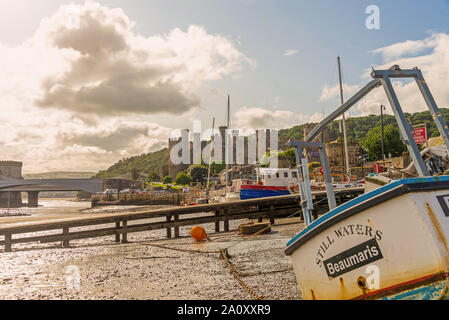 St George's canale a Conwy. Le barche sono arenarsi sulla sabbia e Conwy Castle e un ponte è in background. Un cielo blu con nuvole è sovraccarico. Foto Stock