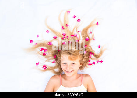 Close up ritratto di adorabile bambina giacente su sfondo bianco con stilizzata lunghi capelli biondi decorato con fiori Foto Stock