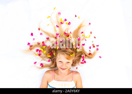 Close up ritratto di adorabile bambina giacente su sfondo bianco con stilizzata lunghi capelli biondi decorato con fiori Foto Stock