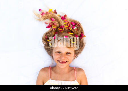 Close up ritratto di adorabile bambina giacente su sfondo bianco con stilizzata lunghi capelli biondi decorato con fiori Foto Stock