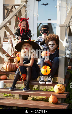 Multi-etnico gruppo di bambini che indossano costumi di Halloween in posa sul portico decorato mentre il trucco o trattare insieme Foto Stock