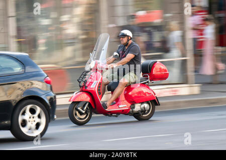 Belgrado, Serbia - 17 Settembre 2019 : un uomo maturo in pantaloncini e maglietta a cavallo di un rosso vintage scooter Vespa in città il traffico della strada, panning s Foto Stock