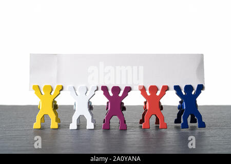 Colorate diverse persone in miniatura statuette in piedi in fila su una pietra scura piastra di ardesia. Intestazione vuota con una copia dello spazio. Isolato su sfondo bianco. Foto Stock