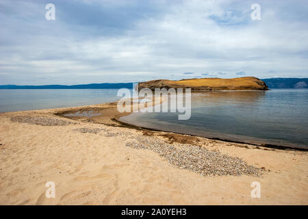 La spiaggia di sabbia del Lago Baikal che si affaccia sulla sabbia sputa e l'isola. Alte montagne sono visibili all'orizzonte. Il cielo di nuvole. Foto Stock