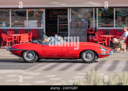 E type Jaguar essendo condotta lungo Marine Parade, Southend on Sea, Essex, Regno Unito nella soleggiata clima autunnale per prendere parte a un'auto show. Cafe con tavoli fuori Foto Stock