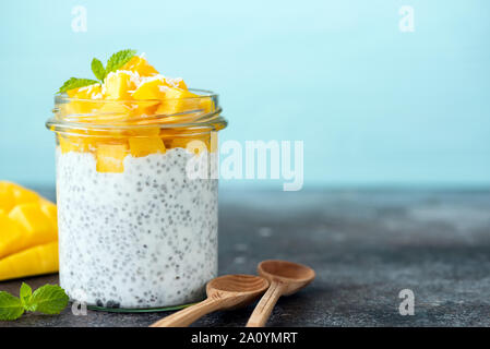 Budino di Chia con mango in barattolo. Cibo sano, vegan dieta vegetariana concetto. Sfondo blu, copia spazio per il testo Foto Stock