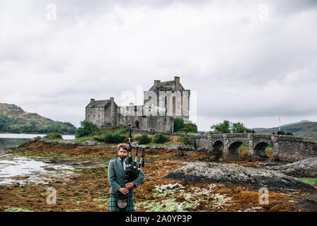 Dornie, Scozia; 27 Agosto 2019: a Scottish bagpiper giocando il suo strumento musicale al di sopra di Eilean Donan Castle Foto Stock