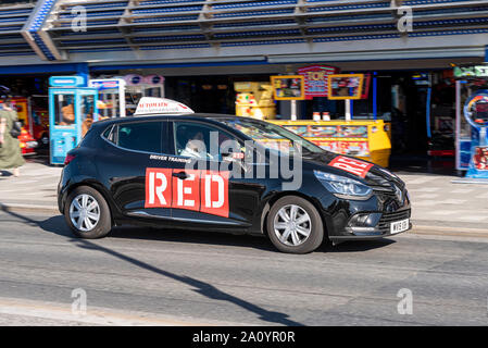 RED Scuola guida lezioni di guida auto essendo azionato da un allievo conducente lungo Marine Parade, Southend on Sea, Essex, Regno Unito passando sale giochi Foto Stock