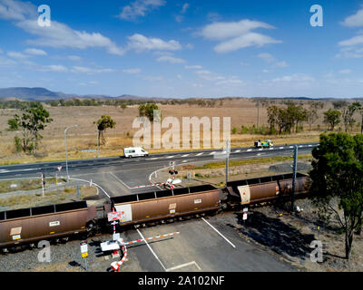 Antenna di treno di carbone con 106 carri passando attraverso un braccio controllato passaggio a livello voce lungo il lato dell'Autostrada di Bruce di Gladstone esportazione termina Foto Stock