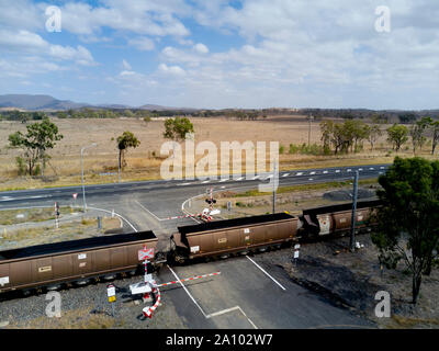 Antenna di treno di carbone con 106 carri passando attraverso un braccio controllato passaggio a livello voce lungo il lato dell'Autostrada di Bruce di Gladstone esportazione termina Foto Stock