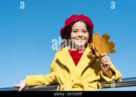 Idee per il tempo libero d'autunno. Bambina adorare la stagione autunnale. Kid tenere foglie di acero. Piccola ragazza indossare abbigliamento cadere all'esterno. Autunno lista della benna per bambini. Cielo chiaro e di buon tempo. Ispirando caduta. Foto Stock