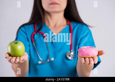 Uno stile di vita sano, cibo e sport concept. Una sana versus malsano. Medico donna mano azienda ciambella e mela verde. Foto Stock