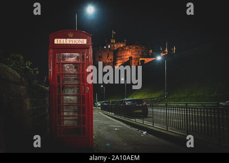 Edimburgo, Scozia, 13 dicembre 2018: il vecchio Britannico rosso phone booth di fianco alla strada di notte con castello in background. Foto Stock