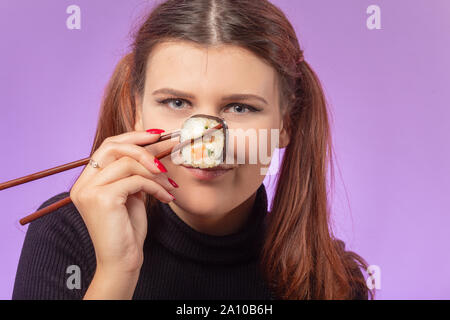 Felice Capelli rossi ragazza mangia sushi su sfondo viola, mostra muso Foto Stock