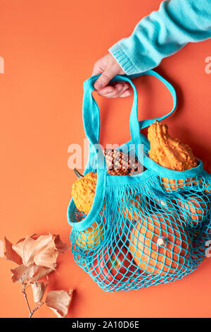 Autunno composizione: stringa di turchese borsa con zucche e mano femminile in blu maglione arancione su sfondo della carta Foto Stock