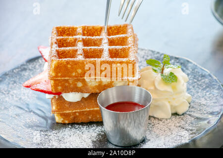 Waffle Strawerry panna fresca nella piastra nera su un tavolo di legno. Foto Stock