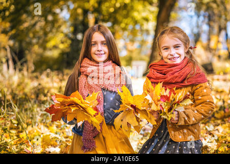 Due graziosi sorridente 8 anni le ragazze a giocare con le foglie in un parco su una soleggiata giornata autunnale. Foto Stock