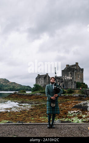 Dornie, Scozia; 27 Agosto 2019: a Scottish bagpiper giocando il suo strumento musicale al di sopra di Eilean Donan Castle Foto Stock