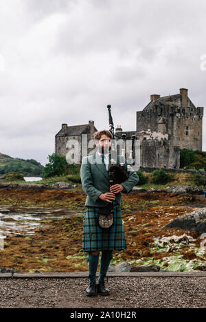 Dornie, Scozia; 27 Agosto 2019: a Scottish bagpiper giocando il suo strumento musicale al di sopra di Eilean Donan Castle Foto Stock