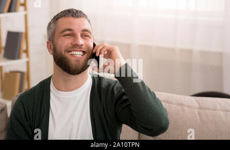 Uomo che parla al telefono cellulare in casa e sorridente Foto Stock
