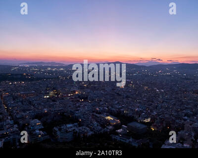 Panorama della città al tramonto. Crepuscolo paesaggio con la città, le montagne e le nuvole sotto i raggi del sole al tramonto. Atene, Grecia. Foto Stock