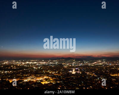 Panorama della città al tramonto. Crepuscolo paesaggio con la città, le montagne e le nuvole sotto i raggi del sole al tramonto. Atene, Grecia. Foto Stock