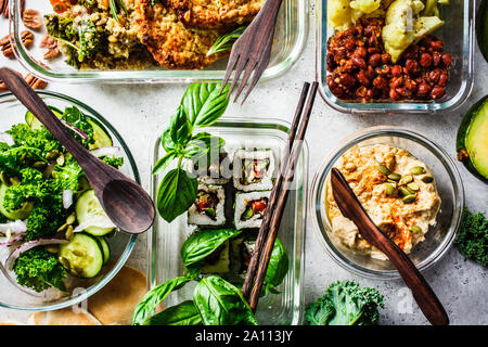 Sano cibo vegan in recipienti di vetro. Lay piatto di spezzatino con ceci, vegan bergrer, hummus, insalata di cavolo, vegan sushi panini e pane. Foto Stock