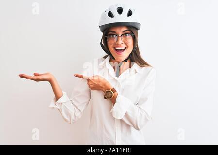 Bella imprenditrice con gli occhiali e il casco protettivo isolato su sfondo bianco stupiti e sorridente alla fotocamera durante la presentazione con la mano e Foto Stock