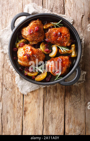Arrosto di cosce di pollo con mele caramellate, mirtilli e rosmarino close-up in una padella sul tavolo. Verticale in alto vista da sopra Foto Stock