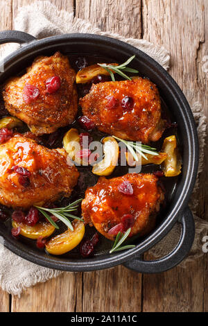 Gustosa piccante di cosce di pollo al forno con mele, mirtilli e rosmarino close-up in una padella sul tavolo. Verticale in alto vista da sopra Foto Stock