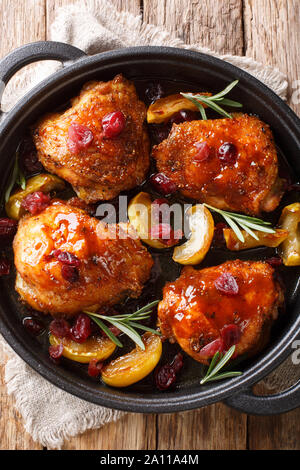 Cotto al forno cosce di pollo con mele, mirtilli e rosmarino in una padella sul tavolo. Verticale in alto vista da sopra Foto Stock