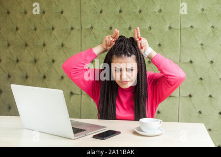 Ritratto di aggressivo arrabbiato giovane ragazza freelancer nero con dreadlocks acconciatura in rosa camicetta sono seduti in cafe e di cattivo umore sono demonstr Foto Stock