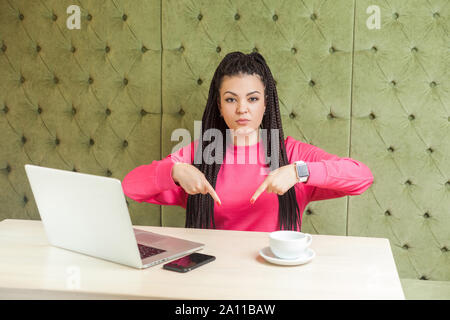 Qui e adesso! Ritratto di angry infelice giovane donna con il nero dreadlocks acconciatura in rosa camicetta, seduta e di cattivo umore sono mostra fing Foto Stock