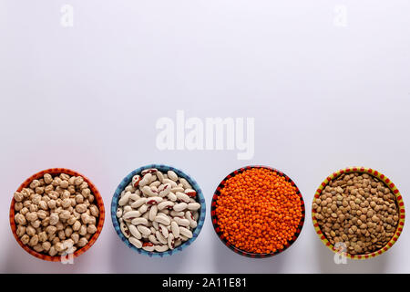 Rosso e marrone di lenticchie, ceci e fagioli bianchi sono i legumi che contengono una gran quantità di proteina sono collocati su uno sfondo bianco in ciotole, orizzontale Foto Stock