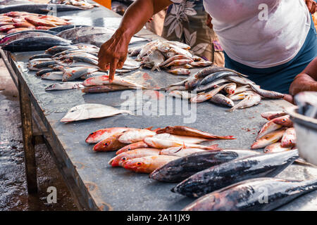 La vendita al dettaglio di pesce sul contatore di sporco al mercato del pesce, intorno alla gente che guarda e scegliere il pesce. Foto Stock