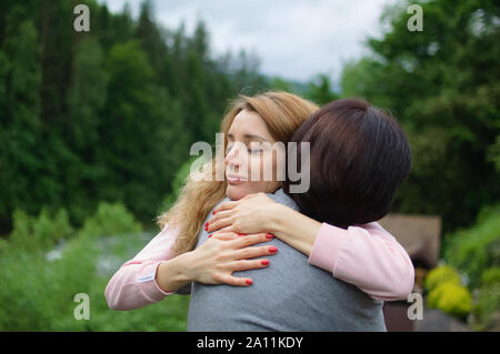Giovane donna bionda è abbracciando il suo anziano madre godendo di essere insieme in montagna durante le vacanze. Concetto di tenerezza, cura, amore familiare, re Foto Stock