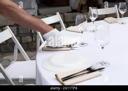 Il cameriere serve il tavolo per banchetti. Tabella di nozze impostazione decorato con fiori e candelabri in ottone con candele. Foto Stock