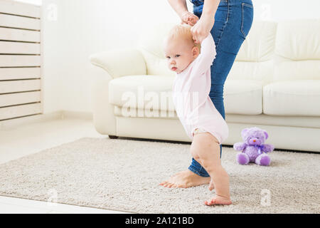 Baby prendendo i primi passi con aiuto-madre a casa Foto Stock