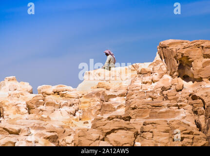 Bedouin seduto sul picco di una alta roccia di pietra contro un cielo blu in Egitto Dahab Foto Stock