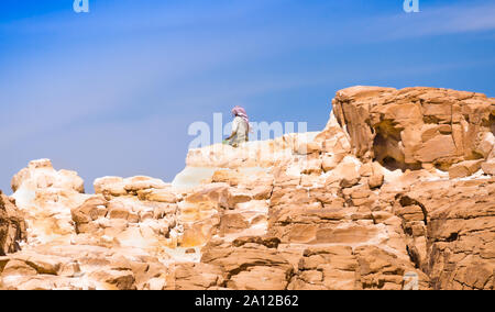 Bedouin seduto sul picco di una alta roccia di pietra contro un cielo blu in Egitto Dahab Foto Stock