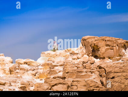 Bedouin seduto sul picco di una alta roccia di pietra contro un cielo blu in Egitto Dahab Foto Stock