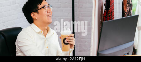 Felice abbigliamento imprenditore godendo e di bere il caffè in ufficio. Giovane uomo asiatico in bicchieri utilizzando un computer e cibo per la consegna Foto Stock