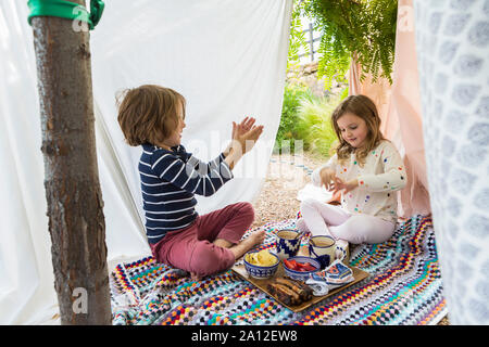 Ragazzo e ragazza che gioca in outdoor tenda improvvisata Foto Stock