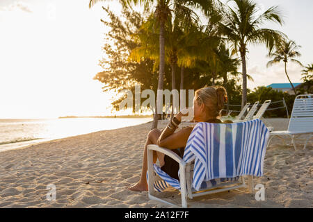 Donna adulta seduto nella sedia spiaggia, Grand Cayman Island Foto Stock