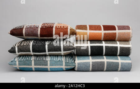 Due pile di coloratissimi cuscini e plaid, su uno sfondo grigio chiaro. Foto Stock