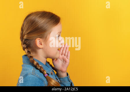 Profilo del bambino in vista laterale. La bambina parla in disparte, tiene una mano in corrispondenza di una bocca. Foto Stock